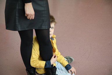 Boy sitting on the floor looking up behind an adult